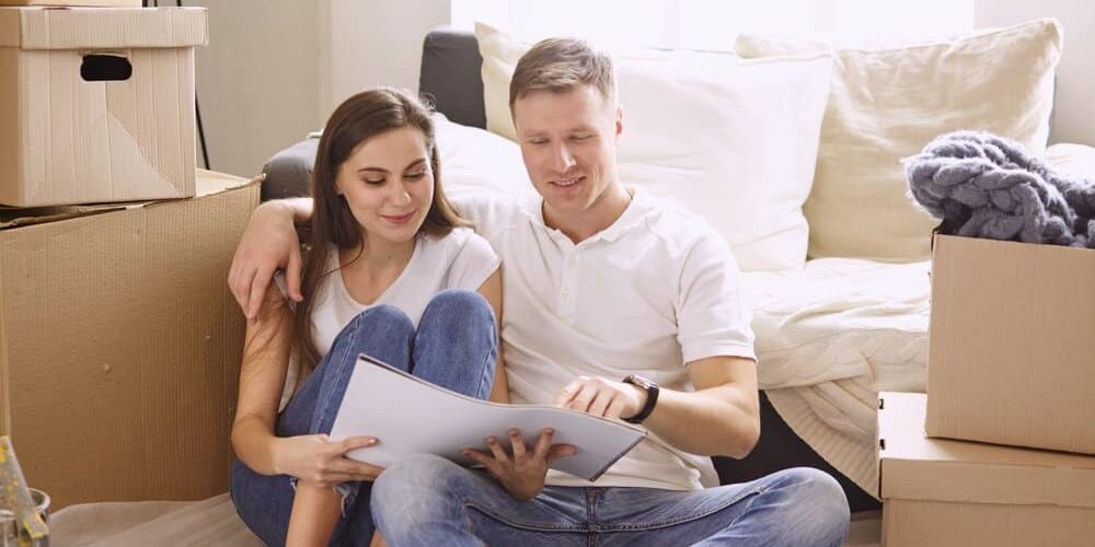 family-planning-renovation young couple looking at blue print of new home remodel surrounded by boxes and belongings