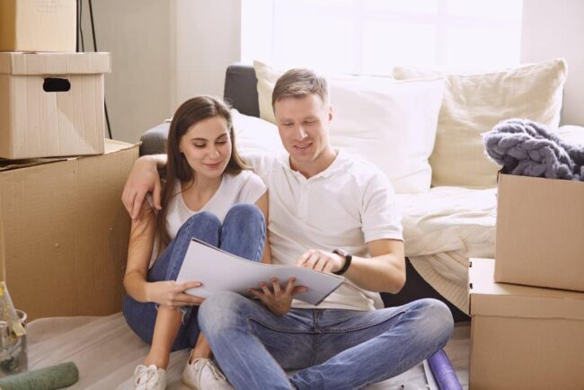 family-planning-renovation young couple looking at blue print of new home remodel surrounded by boxes and belongings